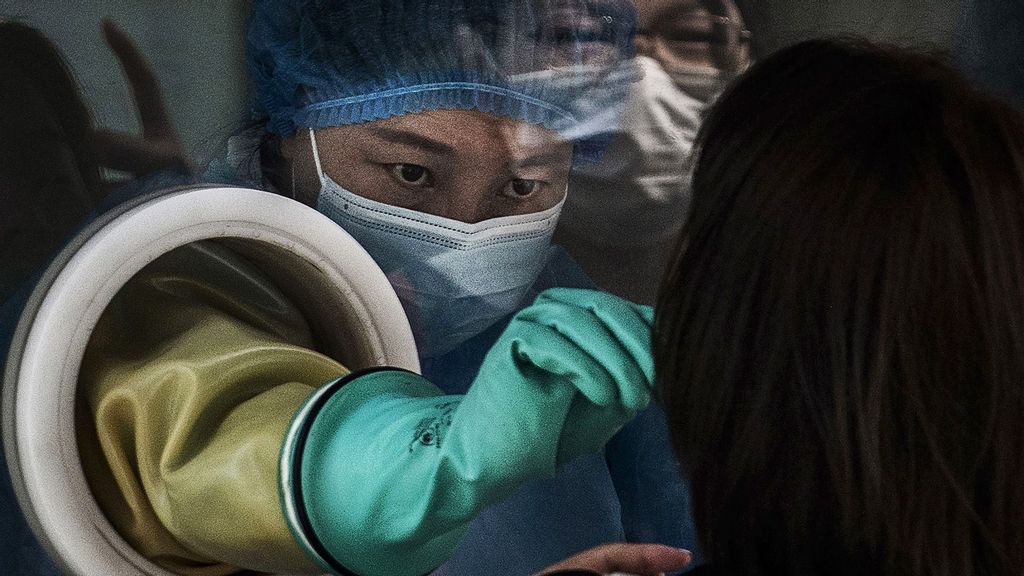 A medical worker wears protective clothing while performing a nucleic acid test on a client from behind glass at a small private testing site on August 6, 2021 in Beijing, China. (Kevin Frayer/Getty Images)